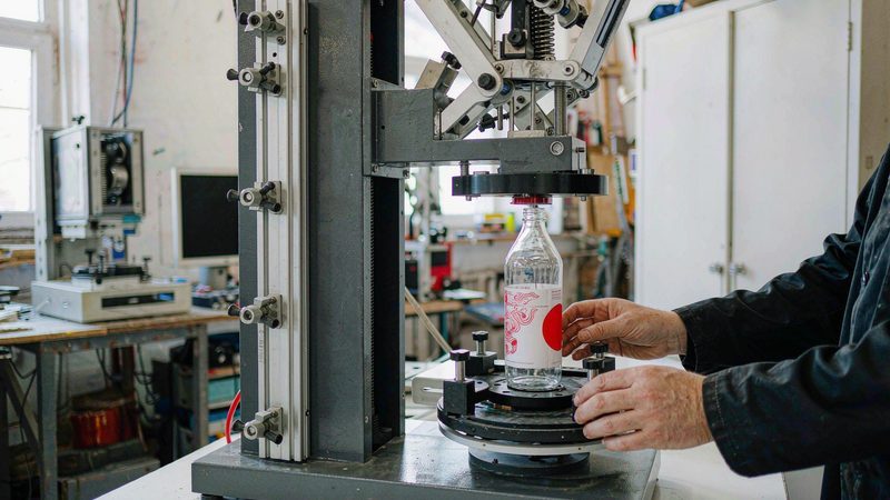Operator loading a glass bottle on a semi-automatic screen printing machine