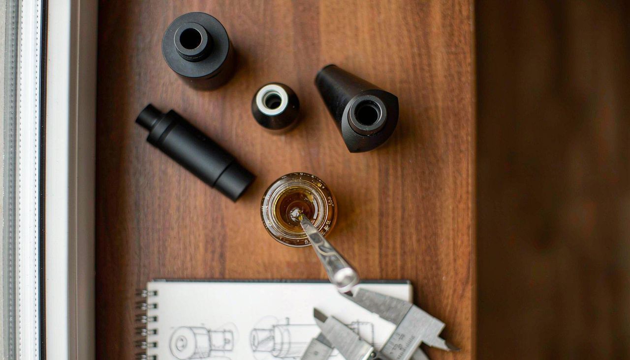 Product development desk with cannabis vape hardware samples, an oil vial, and design sketches