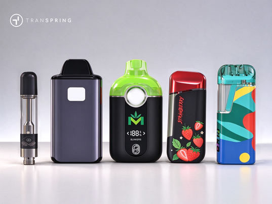Mesa de desarrollo de productos con muestras de hardware para vaporizadores de cannabis, un vial de aceite y bocetos de diseño.