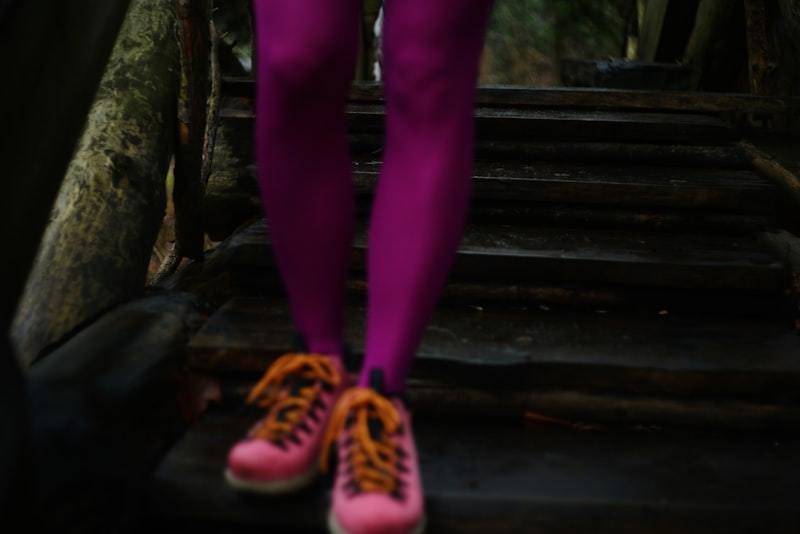 Woman's legs in bright purple activewear leggings paired with pink and orange sneakers on wooden forest stairs to illustrate color-coordinated activewear in use