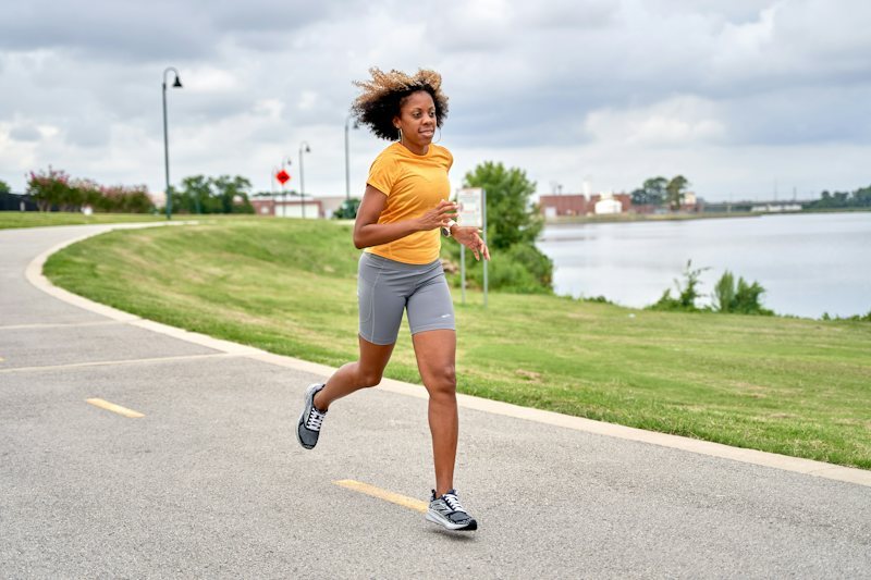 woman running on a road beside a lake wearing loose shell running shorts