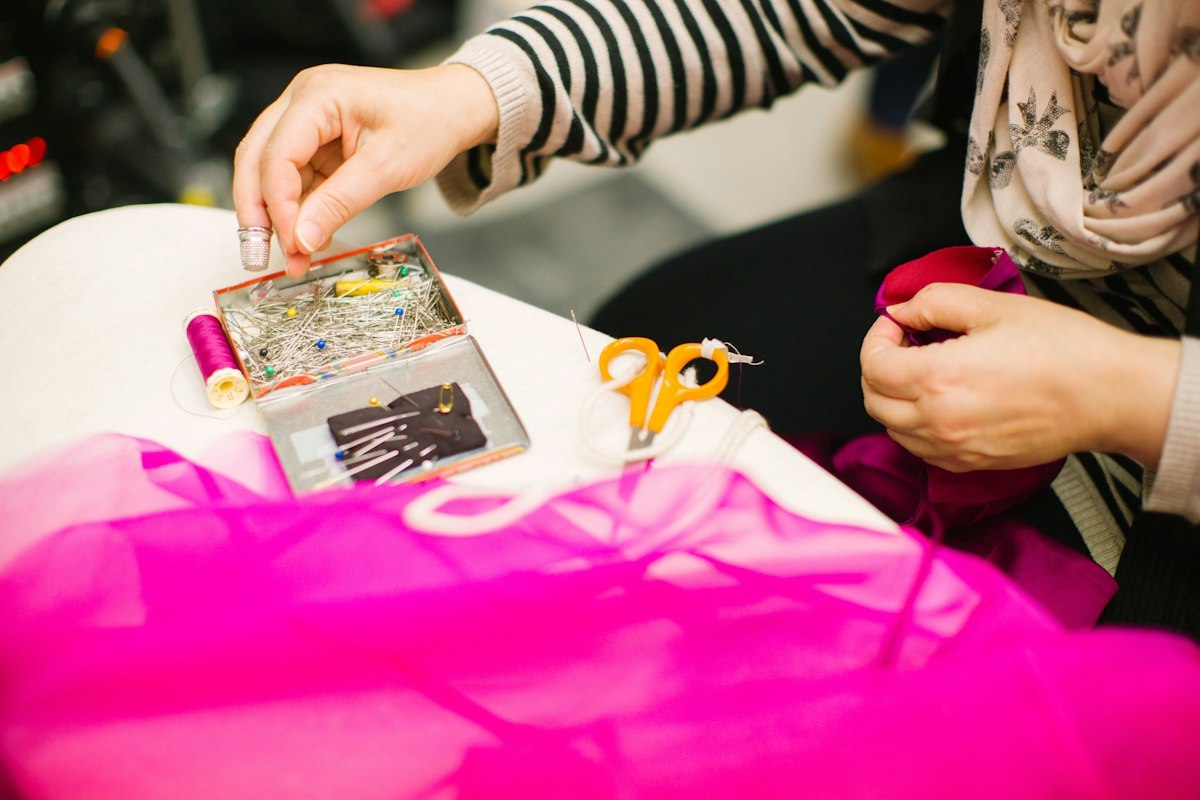 Hands constructing a garment with pins and sewing tools on a work table