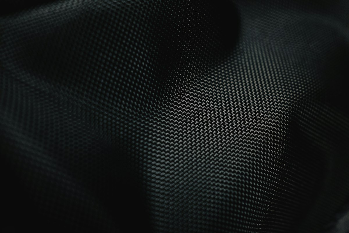 Close-up of a black knitted technical activewear fabric showing how surface sheen concentrates along the knit direction
