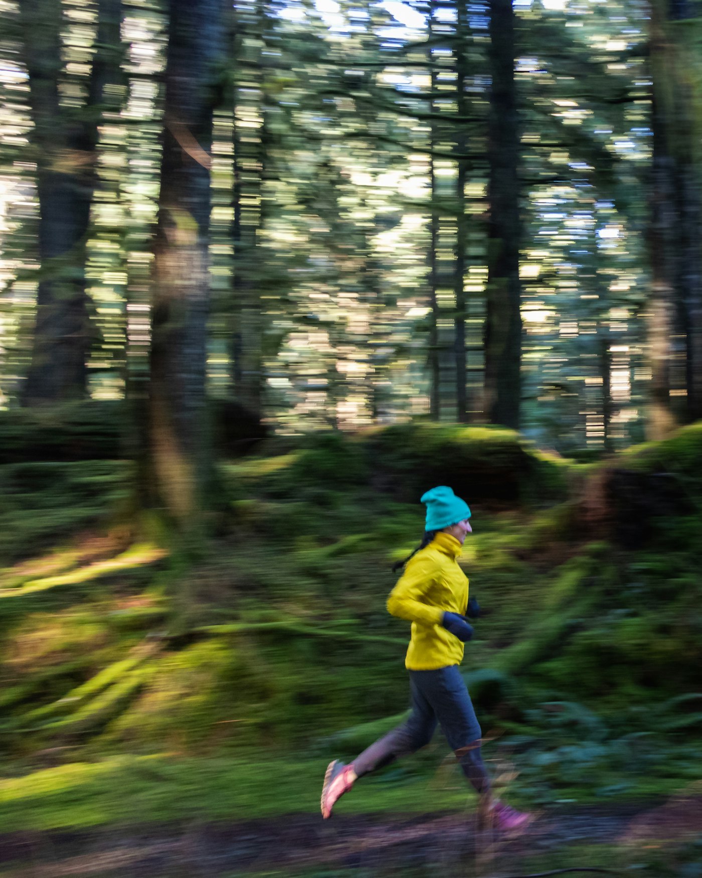 Runner wearing a high-neck long-sleeve layer with gloves and a beanie on a cool-weather forest trail