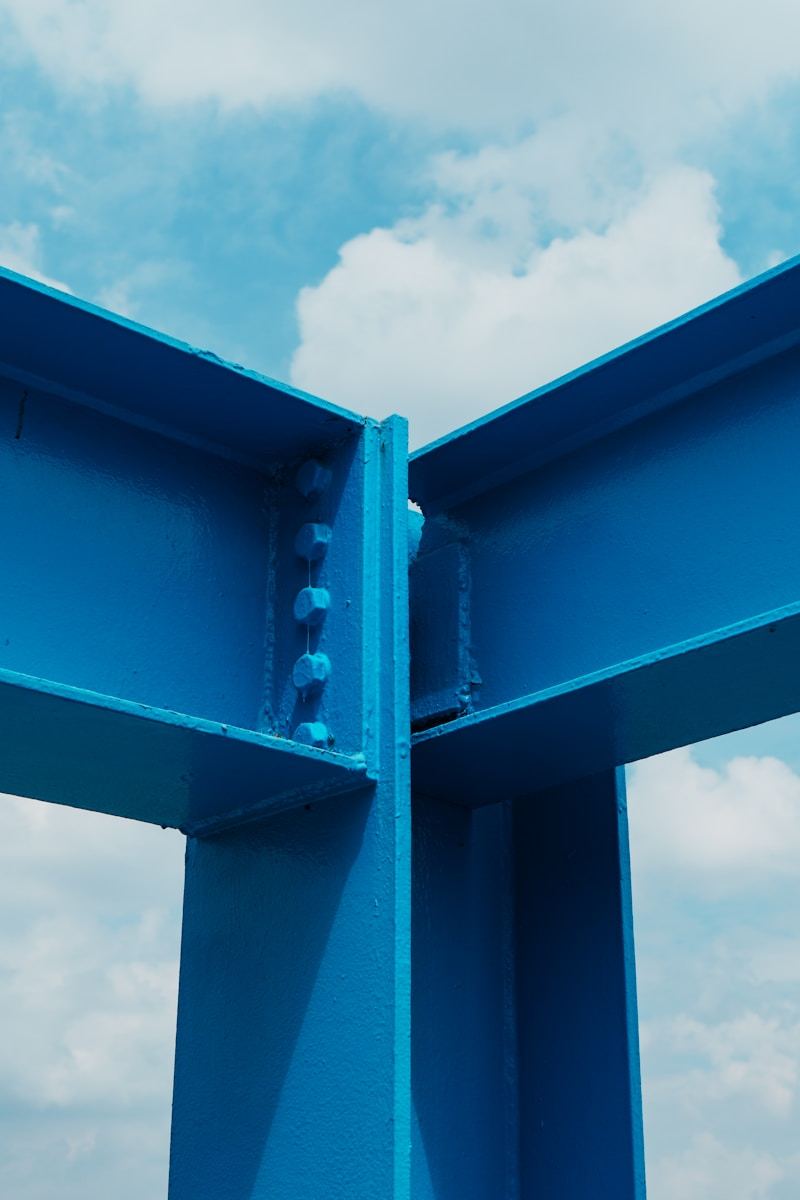 Bright blue powder coated structural steel beams against cloudy sky demonstrating outdoor durability