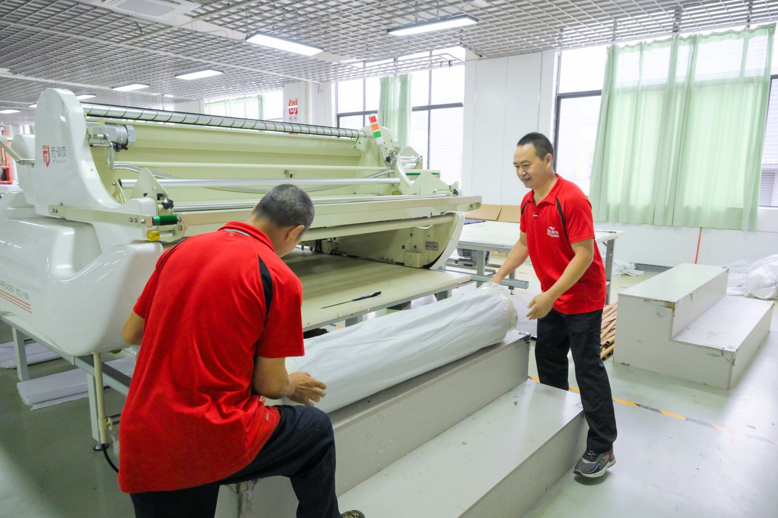 Workers spreading a fabric roll on a spreading table