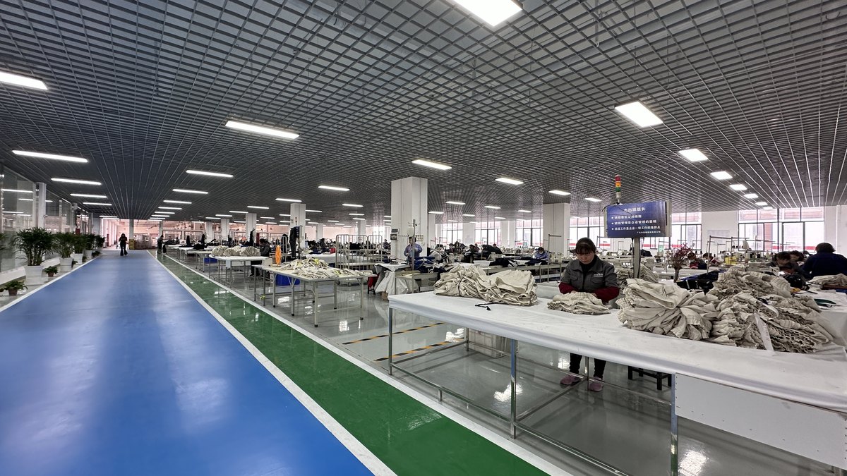 Sewing lines inside the Qianzhan workwear plant, with cut panels staged for assembly