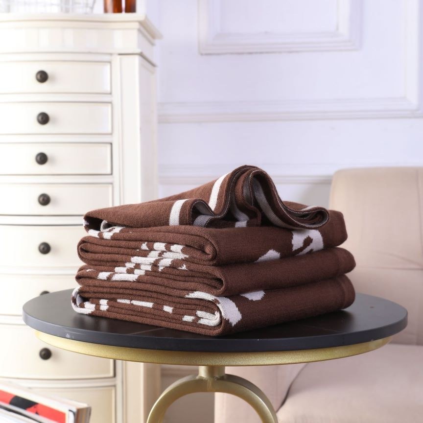 Stack of folded chocolate brown cashmere throws with woven brand labels, styled on a round stool