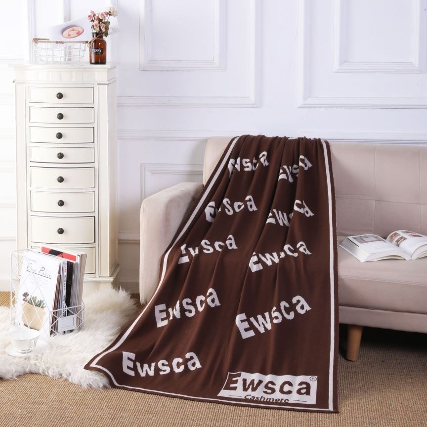 Patterned chocolate brown cashmere throw with a woven brand label, styled over a sofa in a bright room