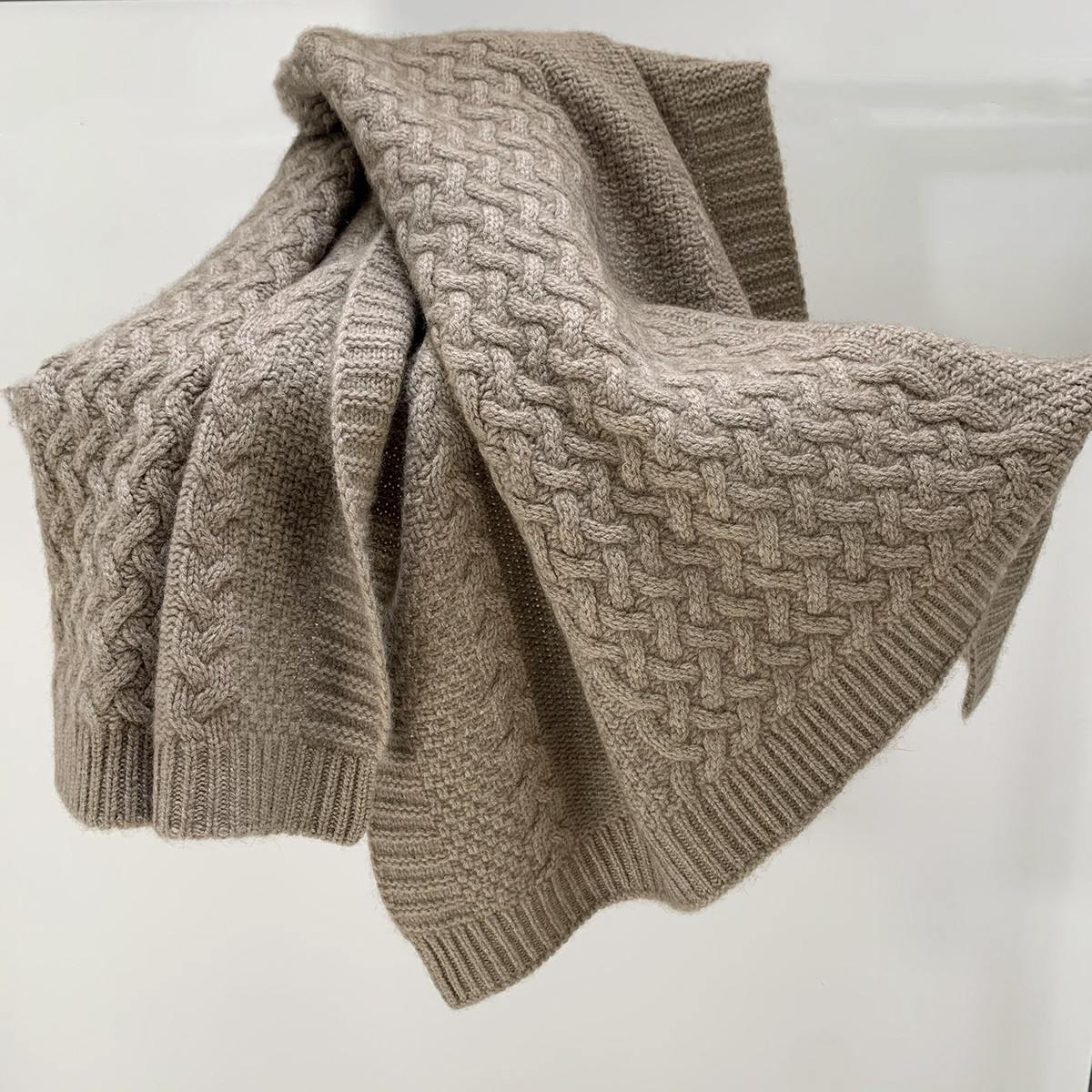 Taupe cable knit cashmere throw folded to show a ribbed border and deep texture
