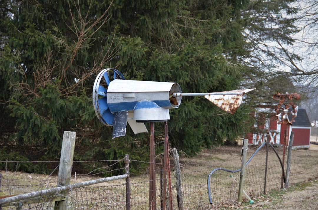 A modern solar fence energizer installed on a wooden fence post in a green pasture