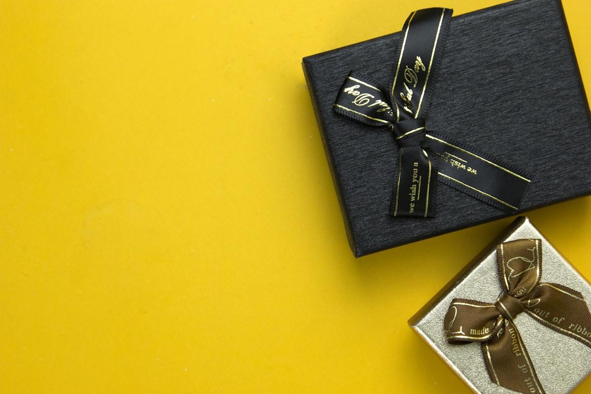 Black magnetic closure perfume gift box with gold ribbon on a coloured backdrop