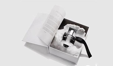 Black magnetic closure perfume gift box with gold ribbon on a coloured backdrop