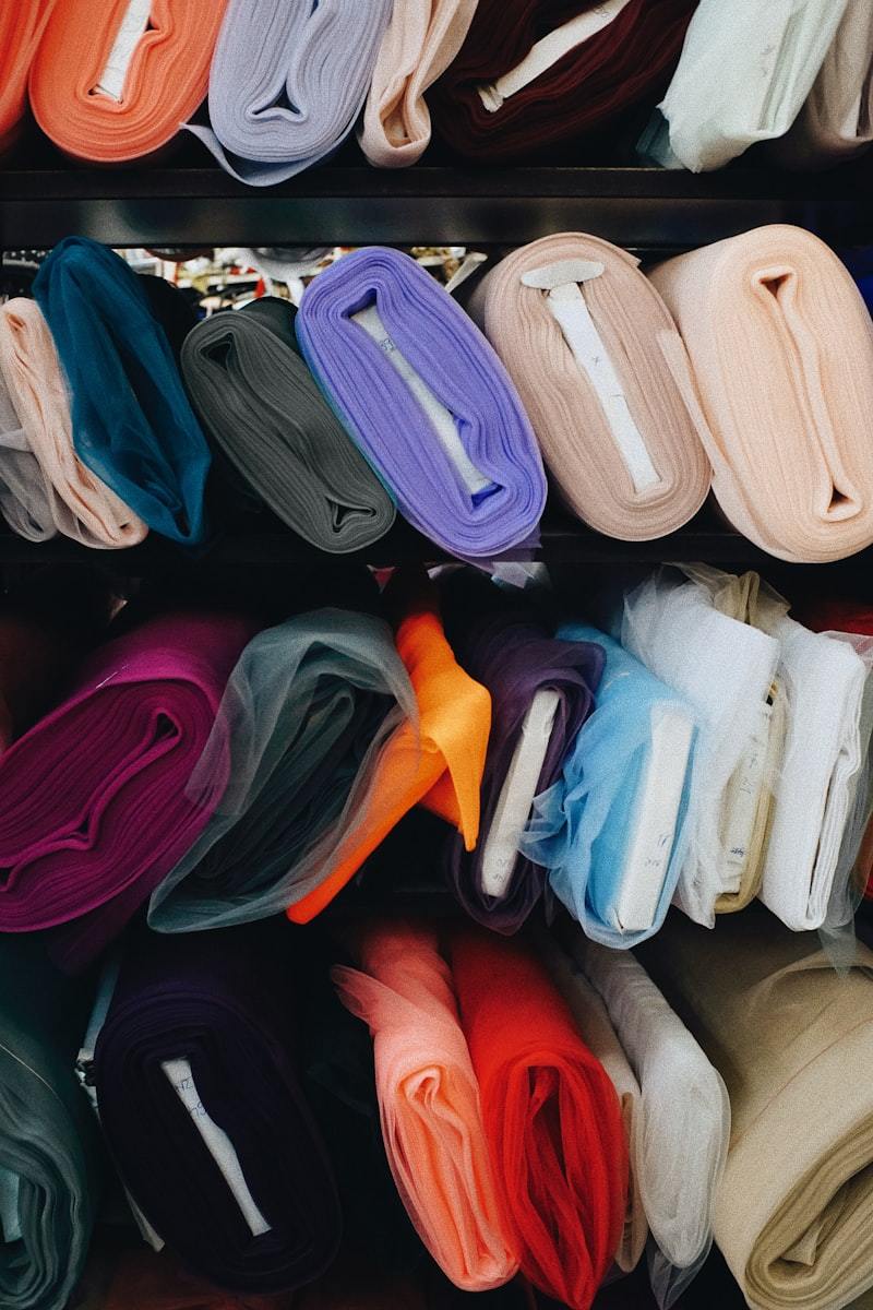 Different colors of cloth stored on a shelf, illustrating dye lot and color consistency management in activewear fabric families