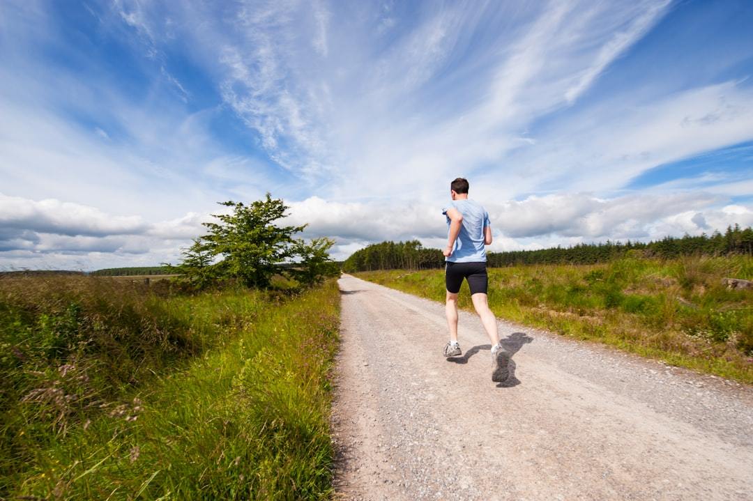 Rear view of a runner moving away down a road, showing the upper back heat and sweat zone a running top must ventilate