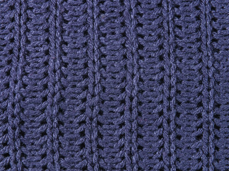 Close-up of a navy blue knitted performance fabric showing visible yarn loops, vertical ribbing and small open gaps that allow airflow through the cloth