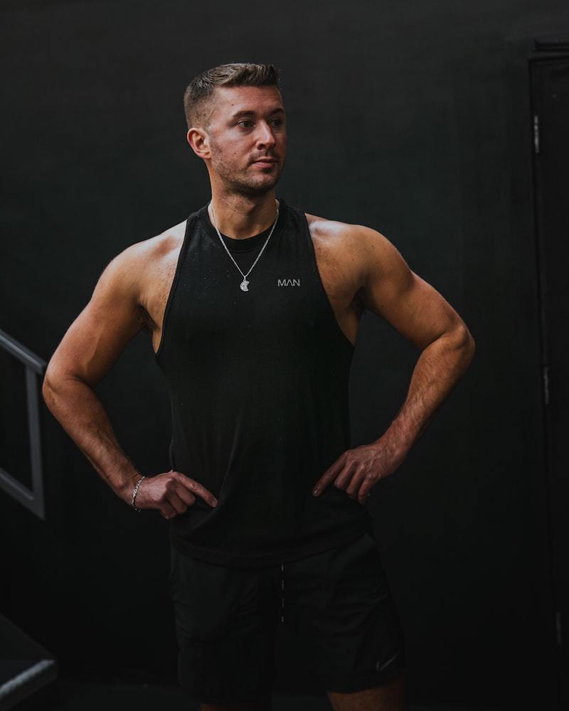 Athletic man in a black sleeveless performance training top standing in a dimly lit gym training area
