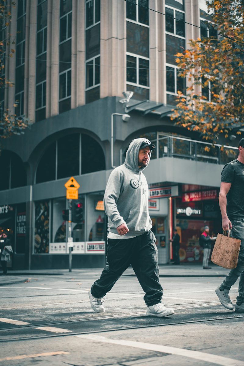 man in hoodie and pants walking on a city sidewalk