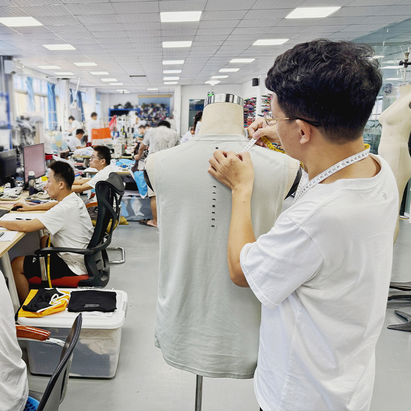 Factory sample room technician measuring a finished men's garment on a mannequin with a tape measure during development review