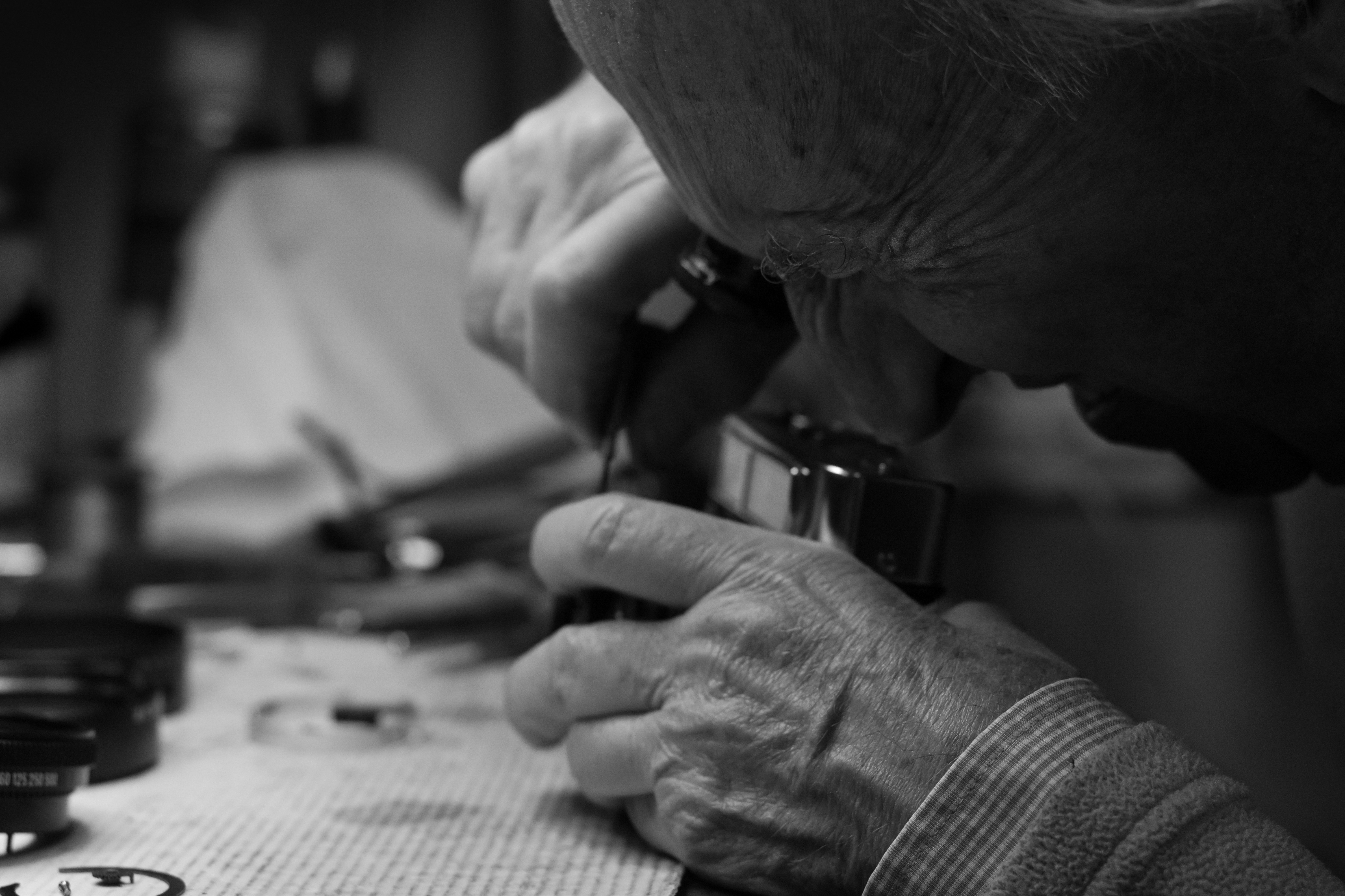 A close-up shot of a jeweler using a loupe to explain the details of a diamond ring to a customer over a counter.