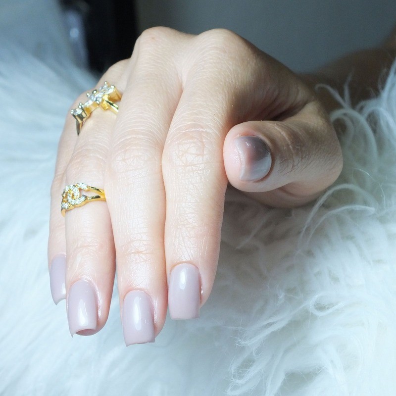 A hand wearing gold plated rings on a white background, examining wholesale jewelry samples from a catalog