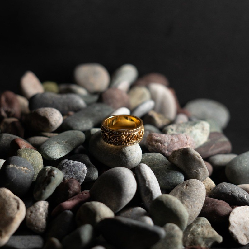 Close-up of a gold plated ring resting on smooth stones, showing plating and stone setting detail