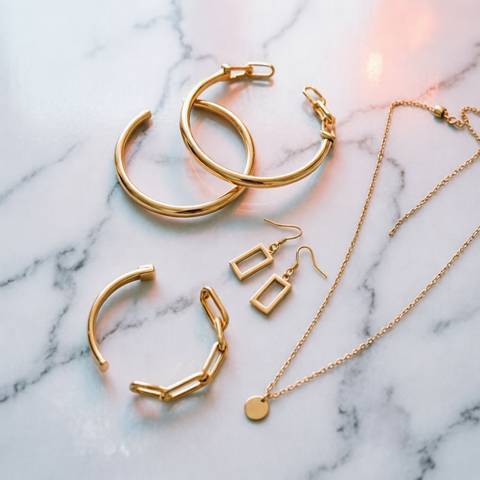 Flat-lay of gold plated jewelry: hoops, square studs, chain