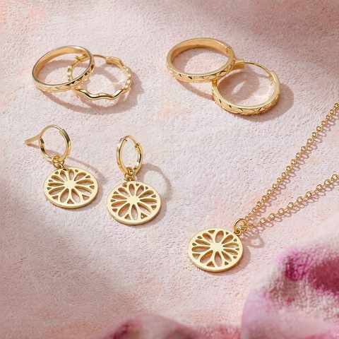 Flatlay of trendy 18K gold plated rings, earrings and a pendant on a blush surface