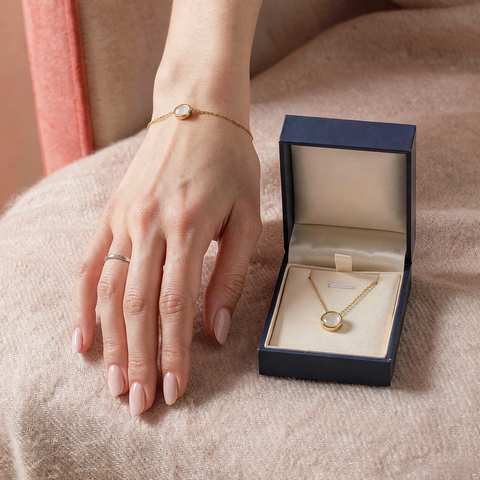 A delicate gold plated bracelet worn on the wrist beside a jewelry gift box
