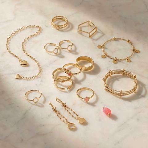 An assortment of gold plated rings, bracelets and earrings arranged on marble
