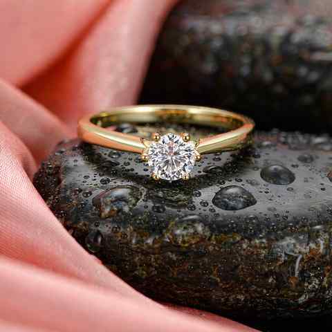 Gold plated ring with a clear CZ stone resting on a wet stone surface with water droplets
