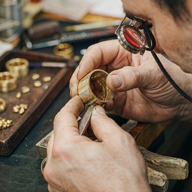 Artesano inspeccionando una pieza terminada de joyería chapada en oro bajo luz de taller