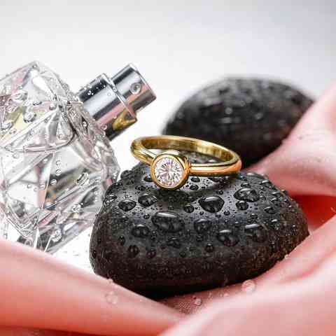 Gold plated CZ ring beside a perfume bottle and water droplets showing common tarnish triggers
