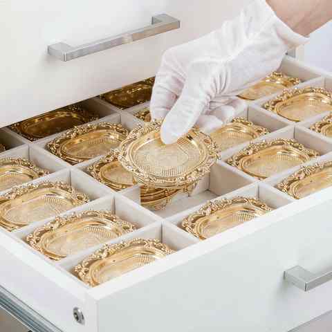 Gloved hand lifting a gold plated jewelry tray from organised storage