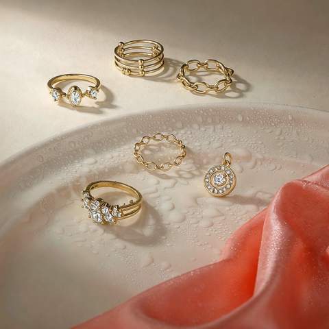 Gold plated CZ rings and pendant beside water droplets and a coral silk cloth