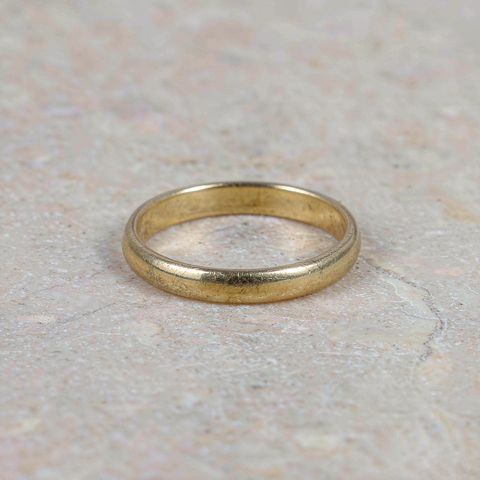 Macro close-up of an 18K gold plated ring resting on a light stone surface in natural daylight
