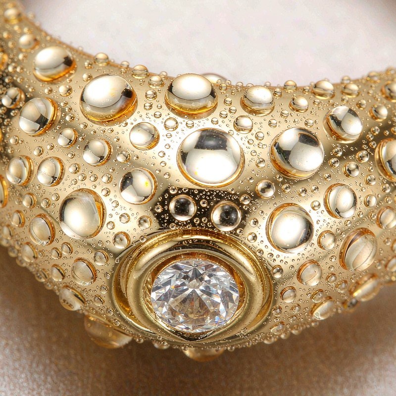 Macro close-up of a gold plated bangle covered in water droplets with a bezel-set cubic zirconia stone