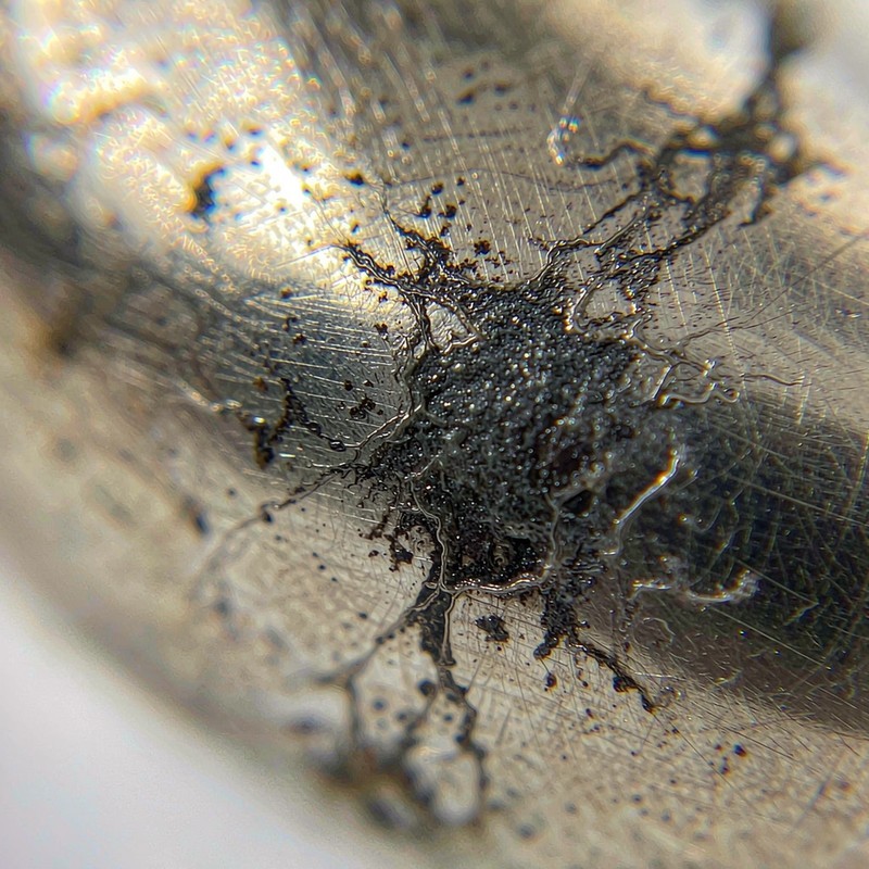 Extreme macro close-up of black oxidation patches spreading across a worn gold-plated metal surface