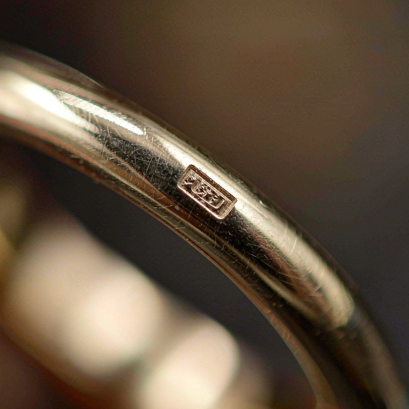 Macro close-up of a tiny engraved hallmark stamped into a gold plated ring band