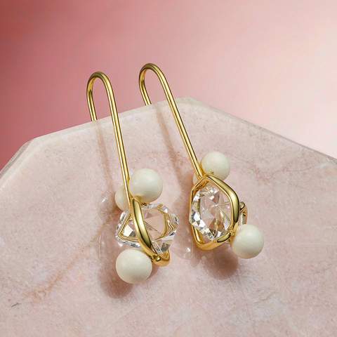 Gold plated drop earrings arranged on a pink marble surface