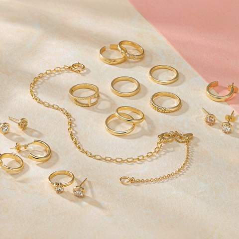 Flat lay of assorted gold plated rings, earrings and necklaces arranged on a soft pastel background