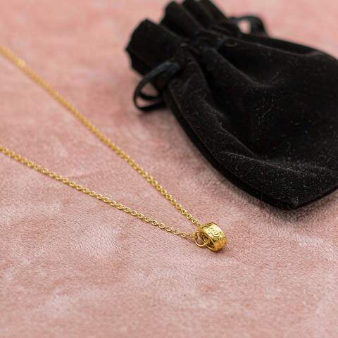 Gold plated necklace stored beside a protective velvet pouch on a soft surface