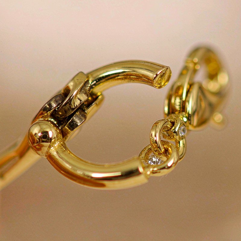 Macro detail of a single 18K gold plated huggie earring hinge and clasp with a clear AAA cubic zirconia accent