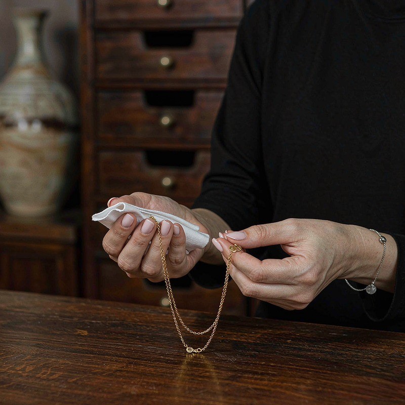Manos limpiando suavemente una joyería chapada en oro 18k con paño de microfibra