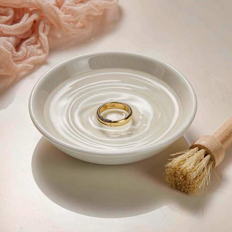Gold plated ring soaking in a bowl of lukewarm water with a soft cleaning brush beside it