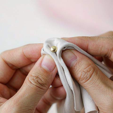 Hands gently drying and polishing a gold plated stud earring with a soft microfiber cloth