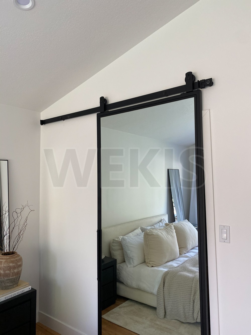 Mirror barn door hung on a black rail above a bedroom opening
