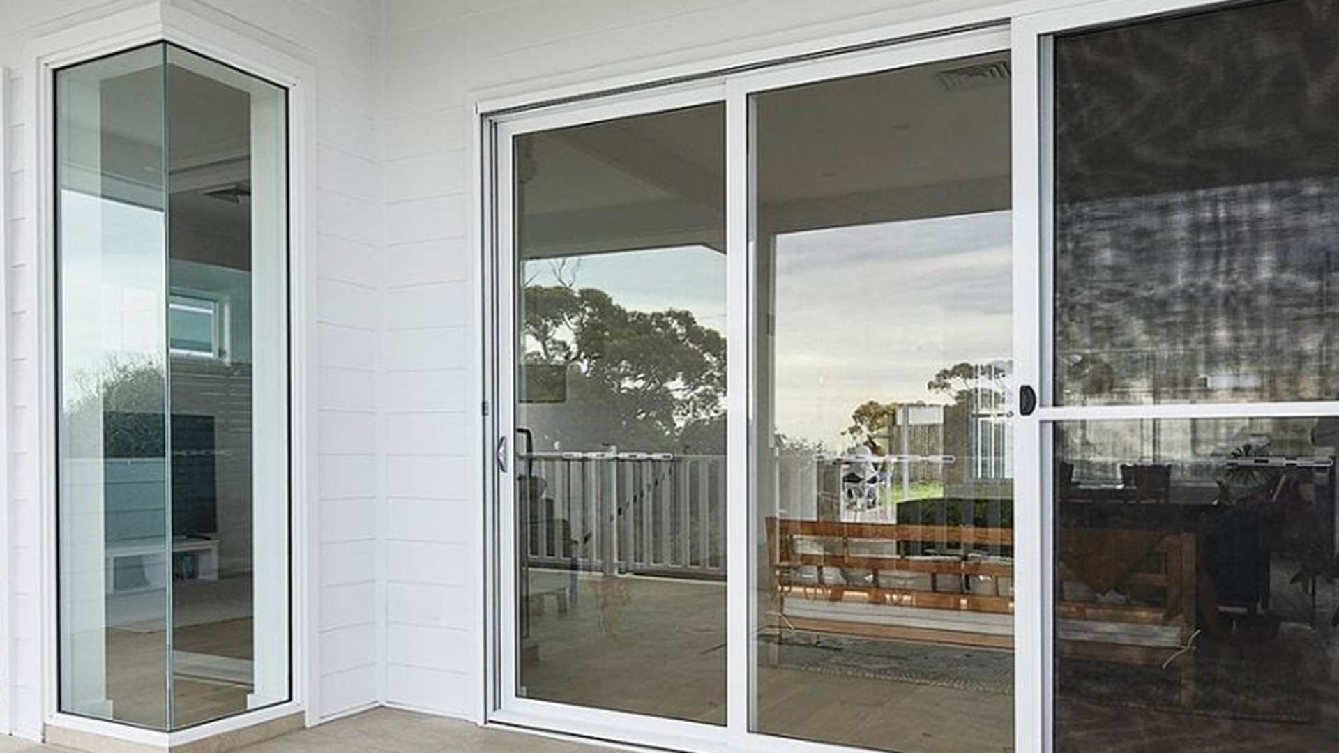 Installed white-framed sliding glass doors and a corner fixed unit, sealed and ready for handover.