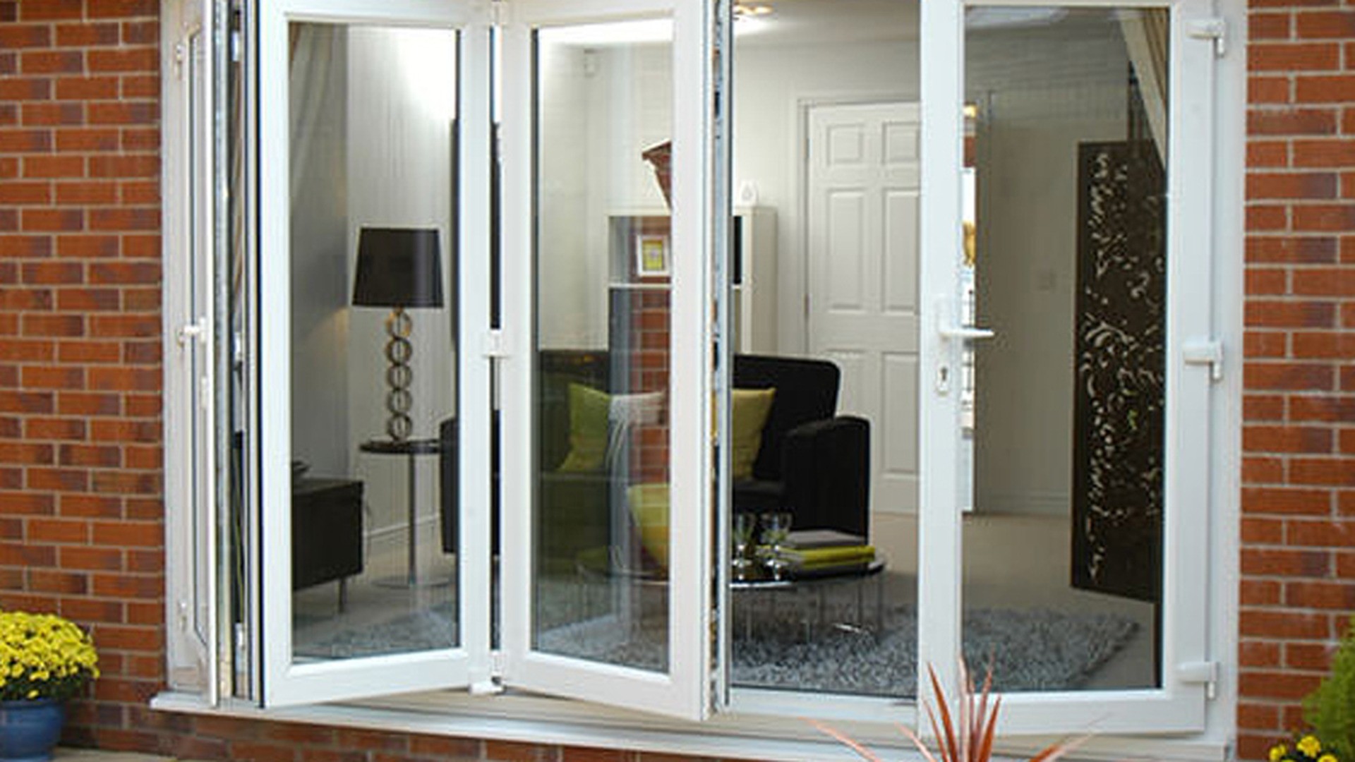 A white folding door set installed on a brick elevation, opening the rear of the house onto a paved patio.