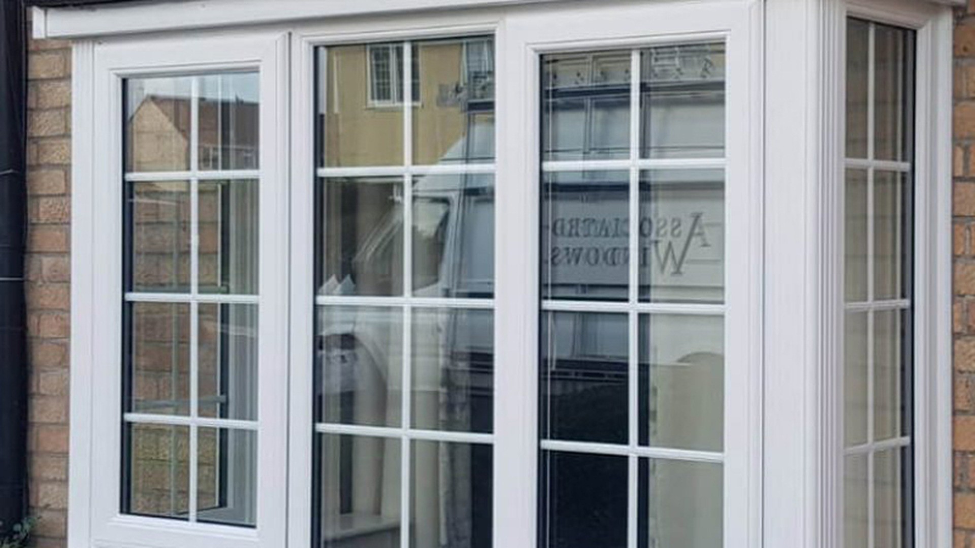 A white uPVC bay window installed on a brick house, shown from the street elevation.